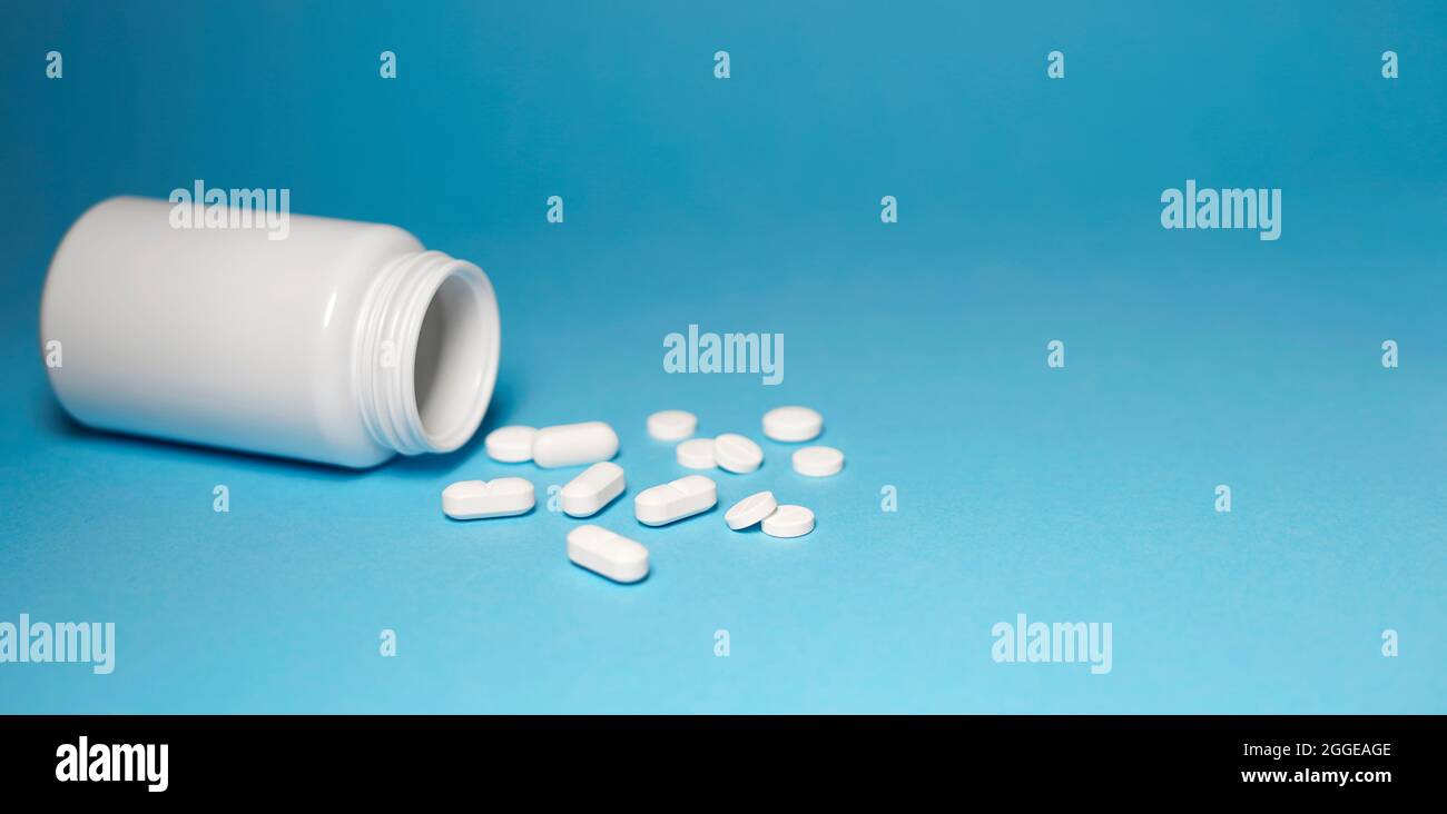 Medicine pills medical and pharmaceutical concept with white tablets bottle and pills scattered on blue background horizontal banner with copy space. Stock Photo