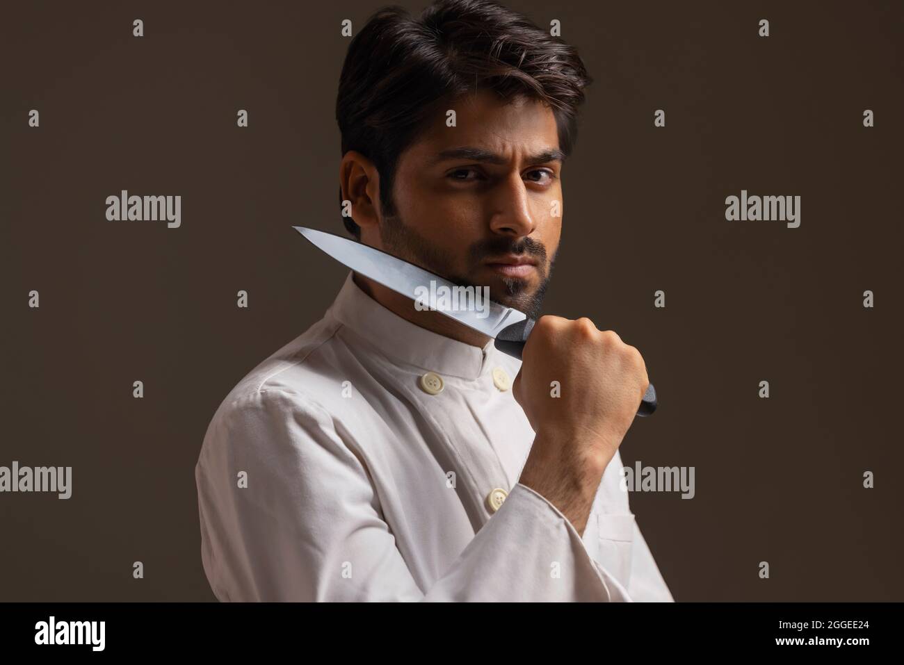 A CHEF POSING IN FRONT OF CAMERA IN SERIOUSNESS WITH KNIFE IN HAND Stock Photo