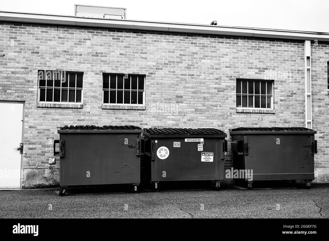 row of covered garbage bins along a brick wall in a back alley Stock Photo