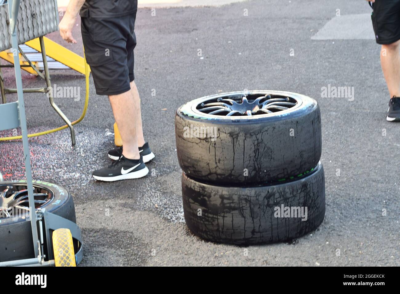 Two stacked racing car tyres and one lying on the floor with 2 men cleaning them Stock Photo