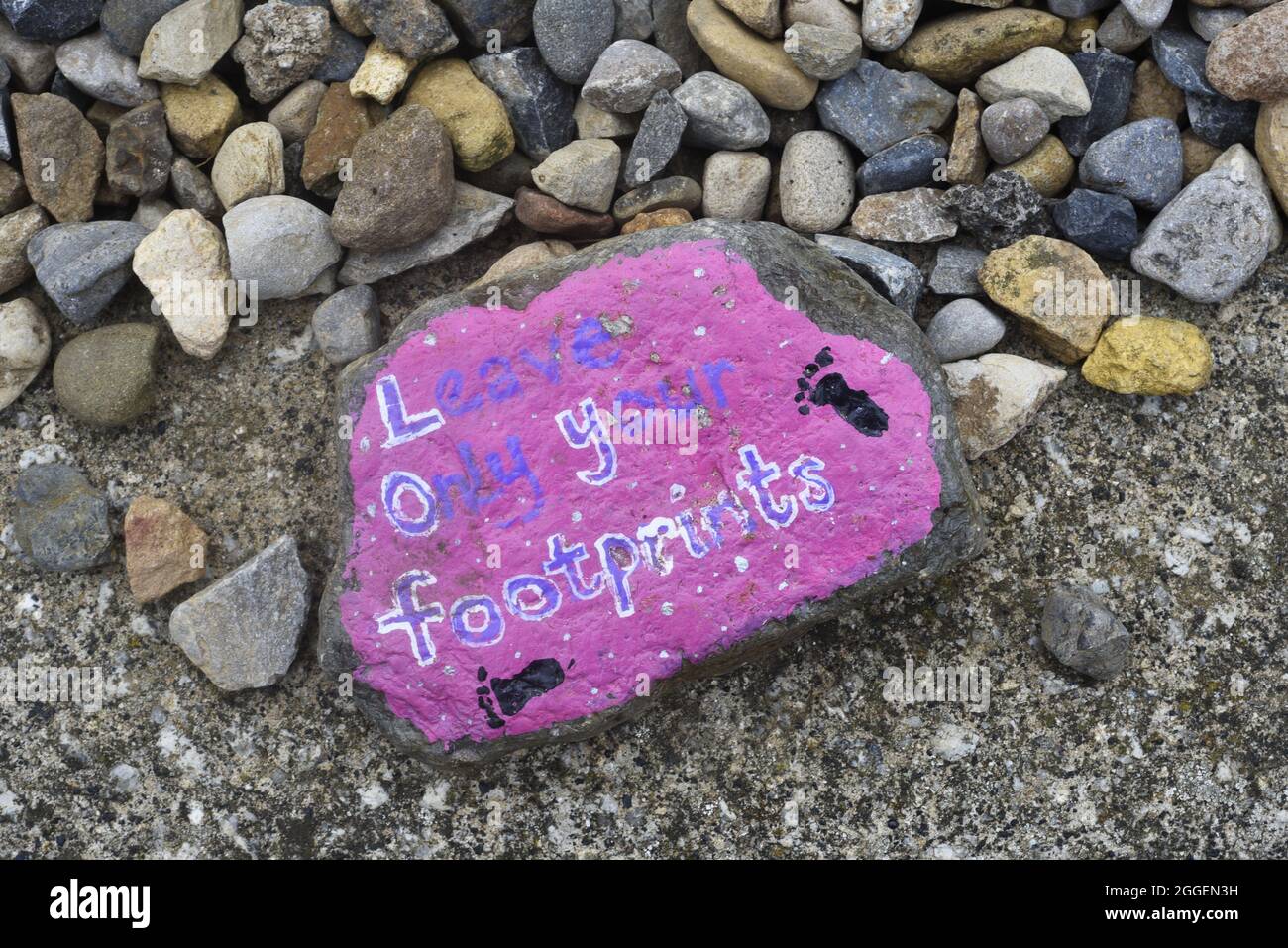 Leave only your footprints, painted on a stone. With footprints on a pink background. On a gravel or stone drive. Environmental concept no people. Stock Photo