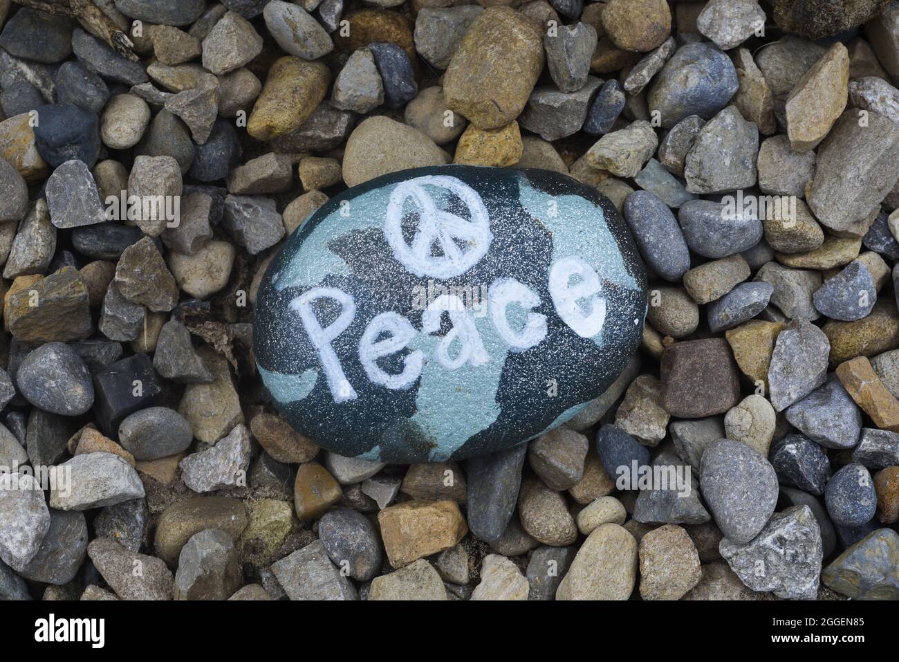 Peace, painted on a stone. With traditional peace symbol on a camouflage background. On a gravel or stone drive. Peace concept no people. Stock Photo