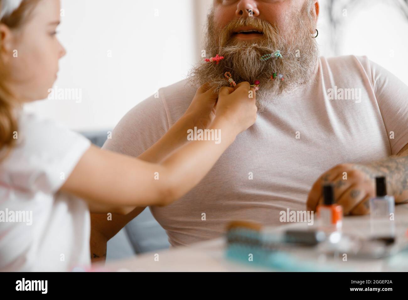 Girl puts colorful scrunchie onto long father beard playing together at home Stock Photo