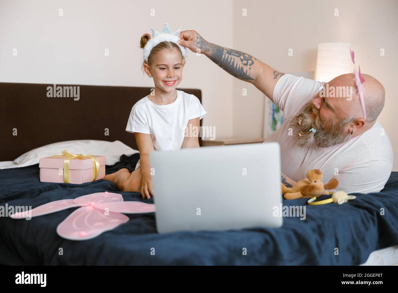 Daddy adjusts headband on head of little girl watching video on large bed at home Stock Photo
