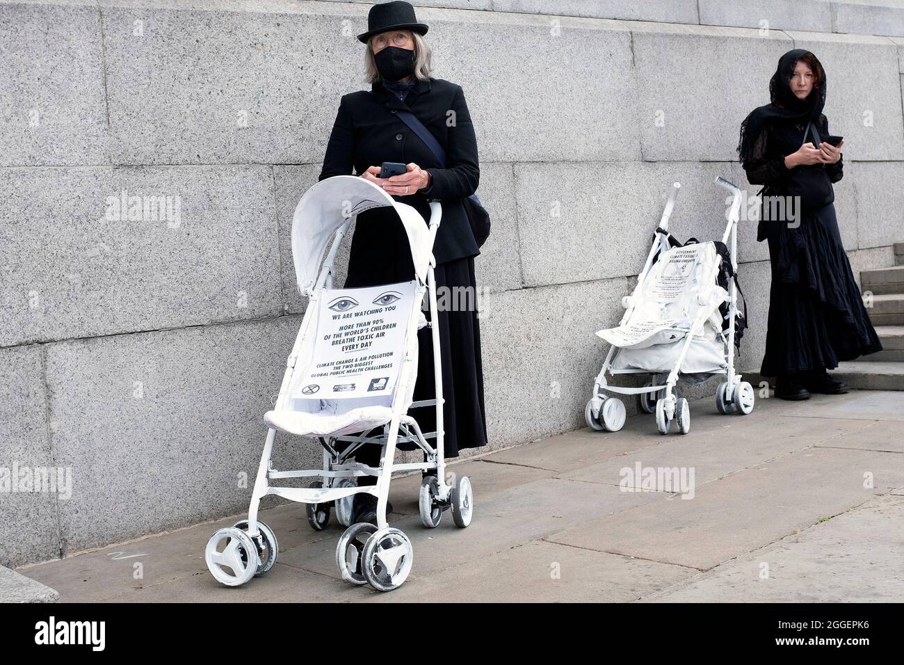 Protestors dressed for a funeral stop to look at their phones as Extinction Rebellion protestors end their Pram Action march at Trafalgar Square. Protestors painted childrenÕs prams white and performed a slow, silent funeral from Parliament Square to Trafalgar Square on the ninth day of their Impossible Rebellion in London, United Kingdom on August 31, 2021. Kieran Riley/Pathos Stock Photo