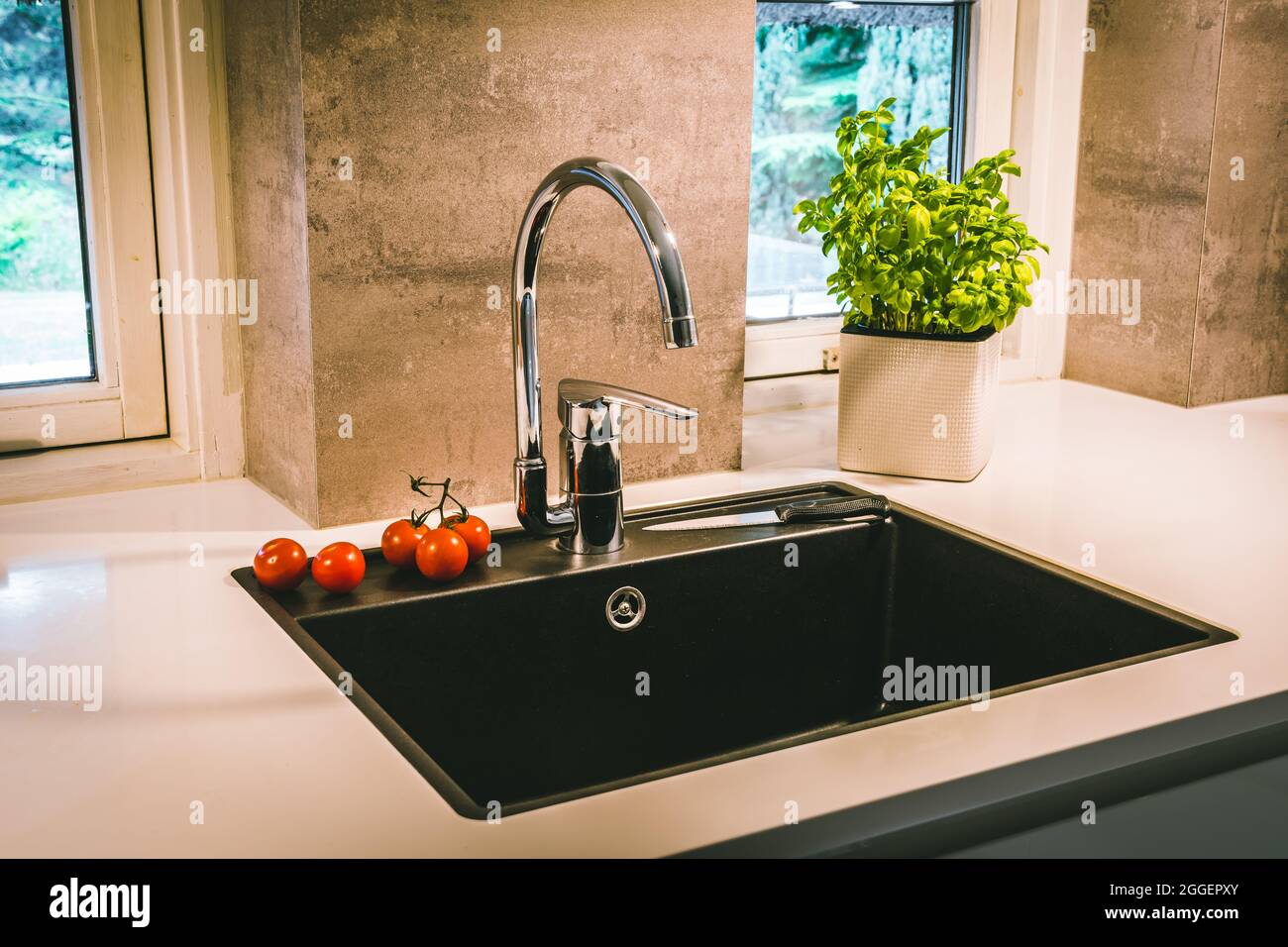 Black sink with chrome fittings in a white worktop in a modern kitchen