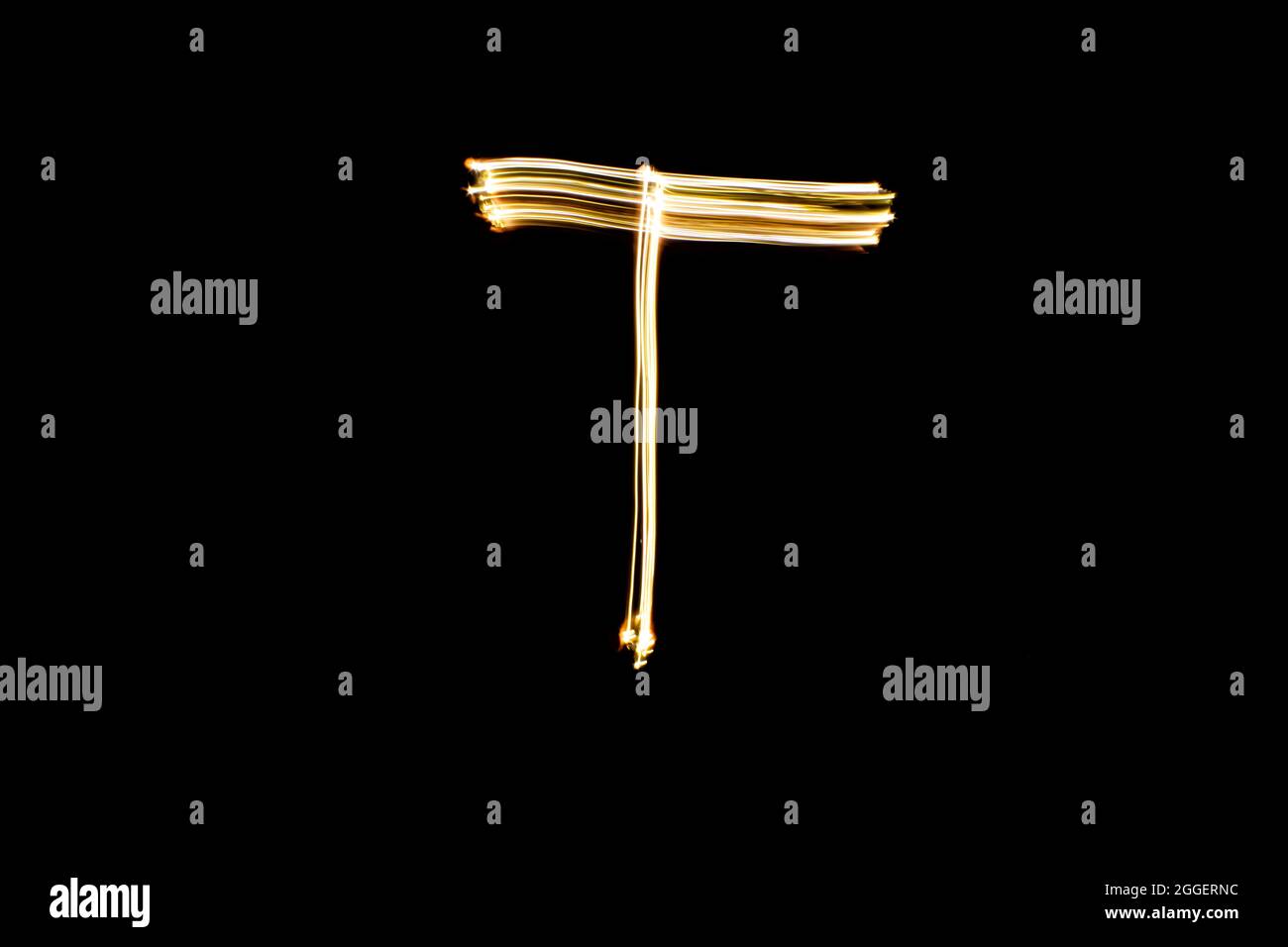 Letter T. Light painting alphabet. Long exposure photography. Drawn letter T with gold lights against black background. Stock Photo