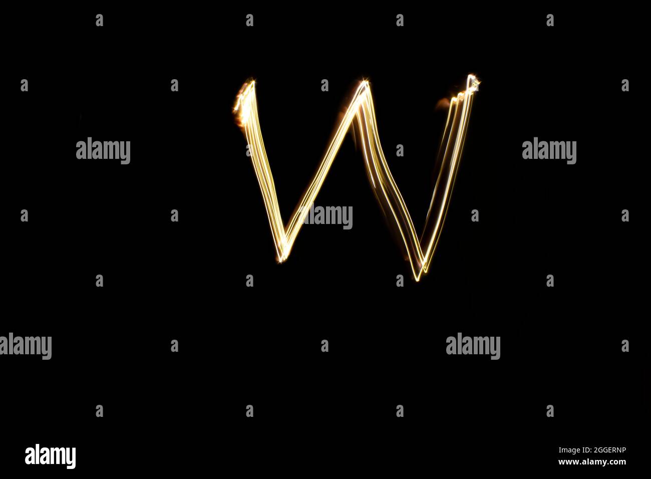 Letter W. Light painting alphabet. Long exposure photography. Drawn letter W with gold lights against black background. Stock Photo