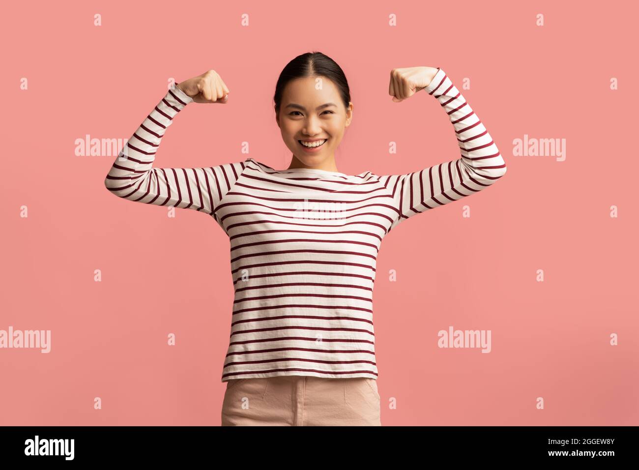 Feminism And Women Power Concept. Portrait Of Strong Powerful Asian Lady Raising Hands And Showing Her Biceps, Positive Korean Female Standing Isolate Stock Photo