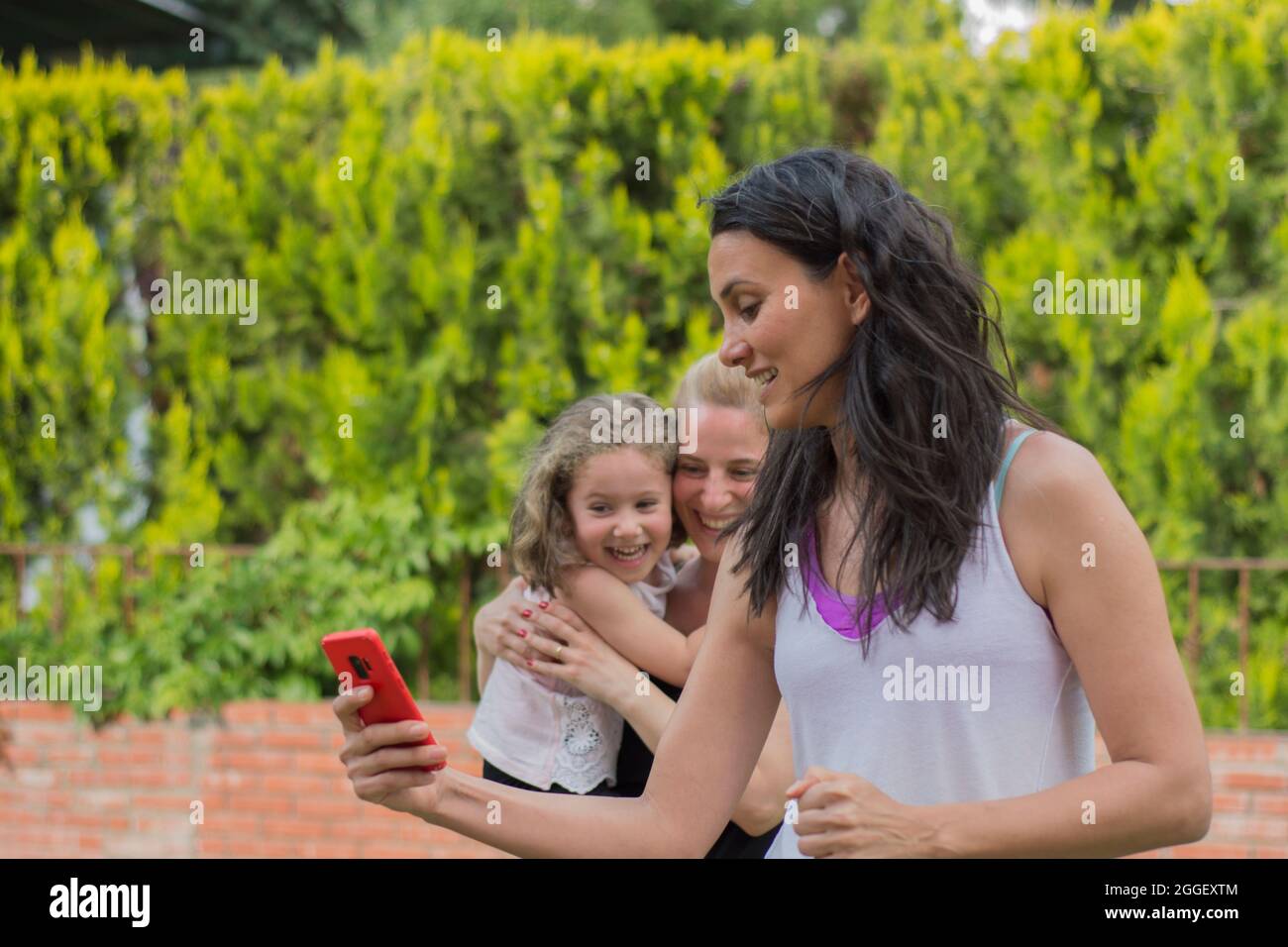 Two young women and a little girlare taking selfies and having fun in the garden of their house. Selective Focus Woman Stock Photo