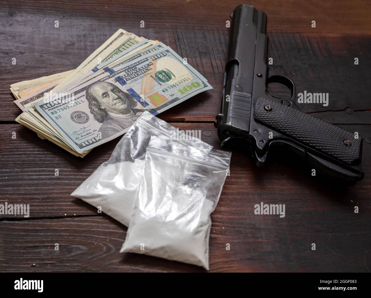 Drugs narcotics illegal business concept. Cocaine plastic packets, pistol and US dollars banknotes on a table. White powder addiction and crime Stock Photo