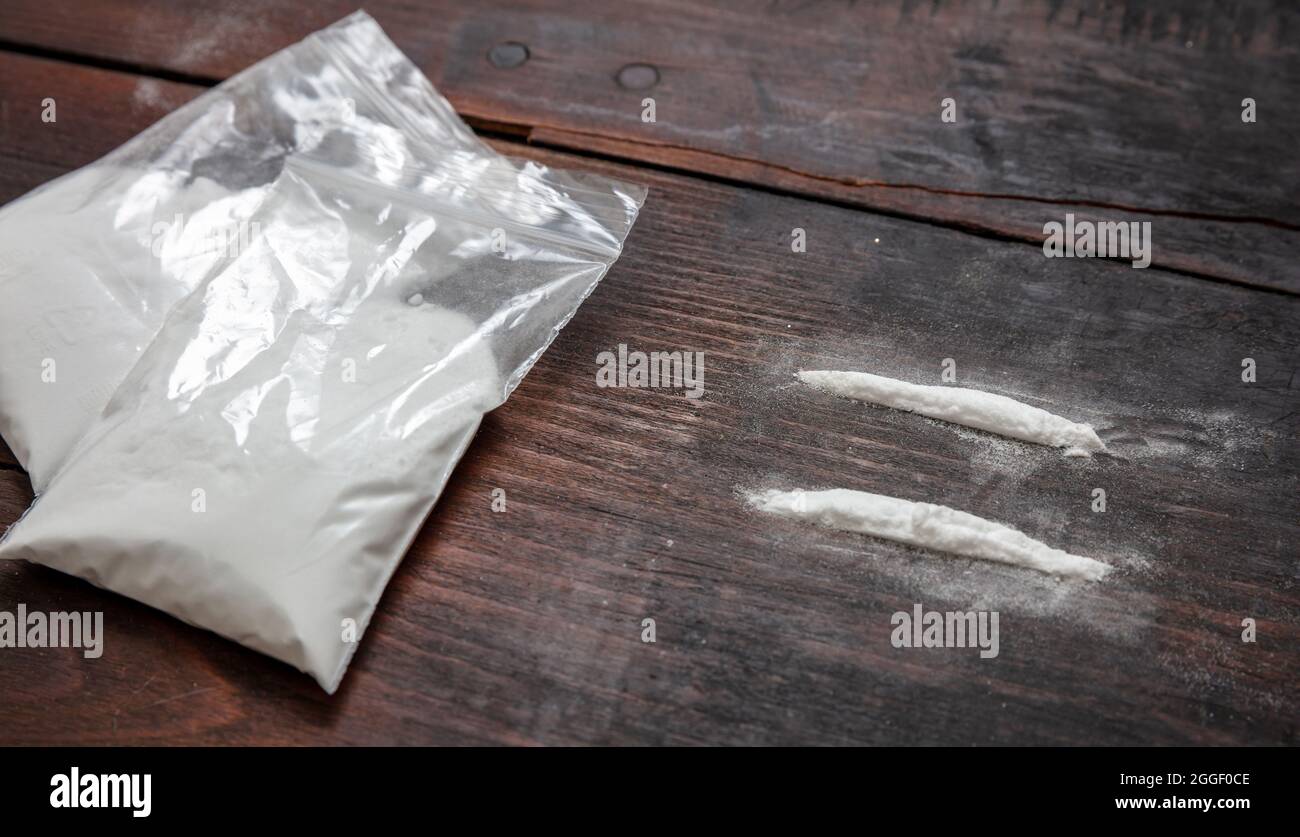 Cocaine plastic packets and two lines. Drugs narcotics addiction concept.  White powder on wooden table background, closeup. Stock Photo