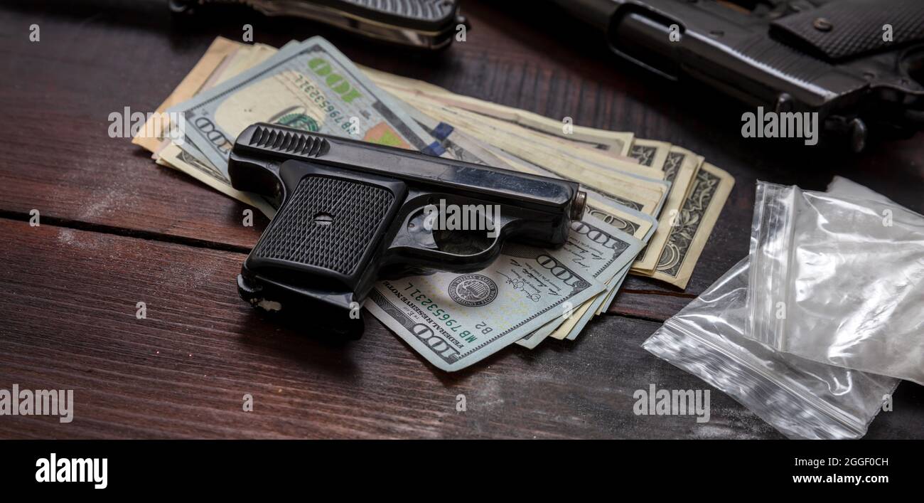 Cocaine plastic packets, guns and US dollars banknotes on a table. Drugs narcotics illegal business concept. White powder addiction and crime Stock Photo