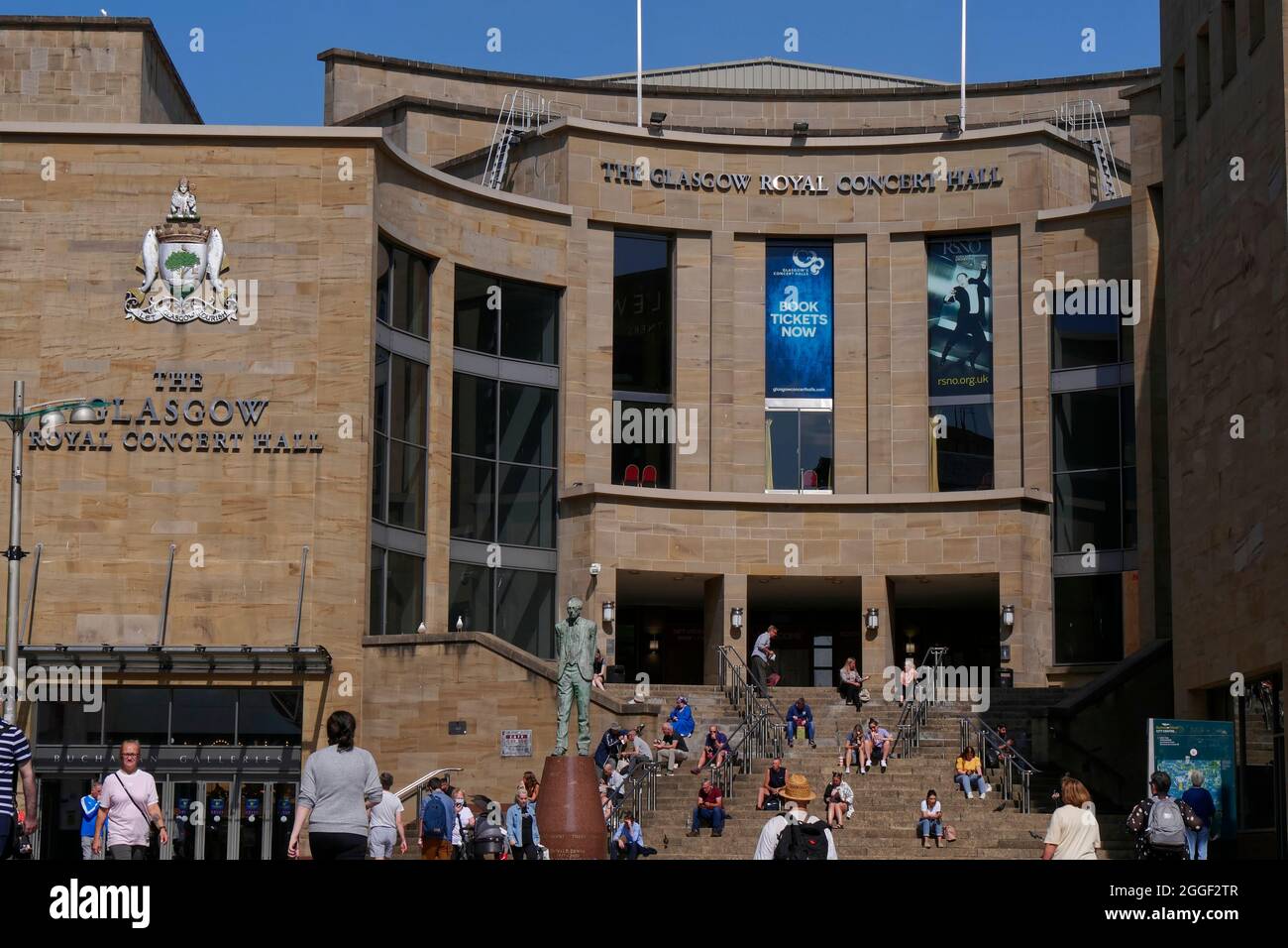people enjoy the sunshine on the steps behind the Donald Dewar statue