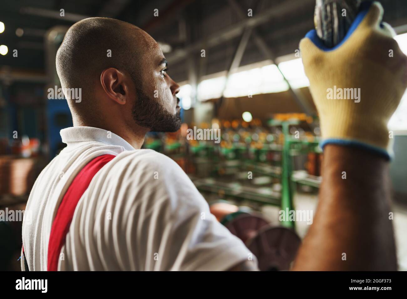 Engineer in uniform using crane controller hanging from ceiling in a factory Stock Photo