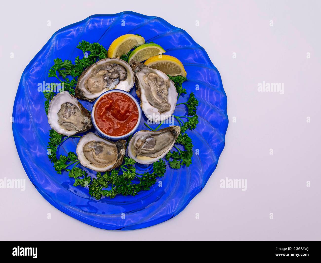 Oyster appetizer served on a round blue plate with colorful garnish  offset on a white background. Stock Photo