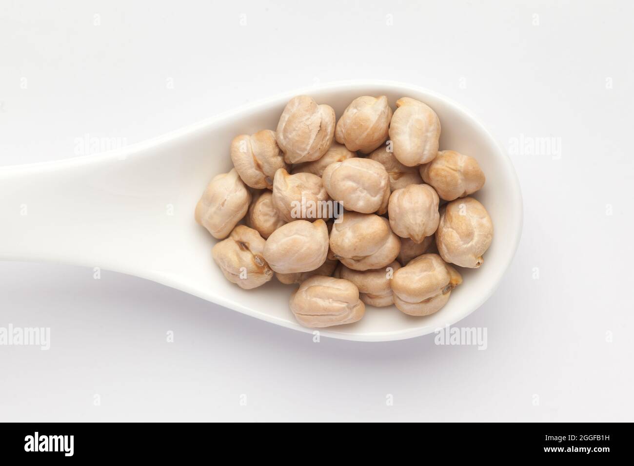Macro Close-up of Organic chhole chana or Kabuli chana (Cicer arietinum) or whole white Bengal gram dal on a white ceramic soup spoon. Top view Stock Photo