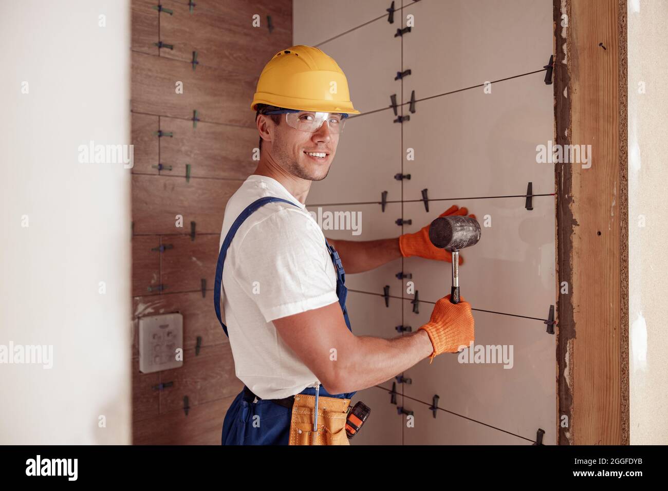 Joyful male builder installing ceramic wall tile in house Stock Photo
