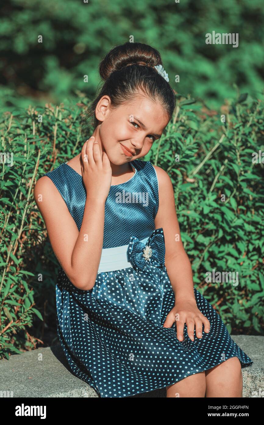 a brunette girl in a blue polka dot dress sitting in the park in the ...