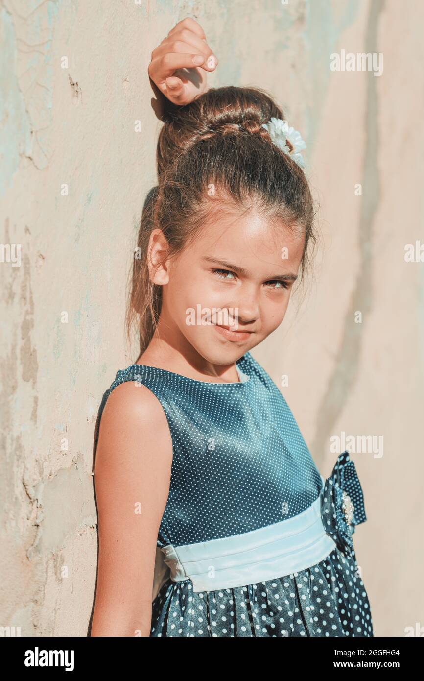 a young brunette girl in a blue polka dot dress stands against the wall ...