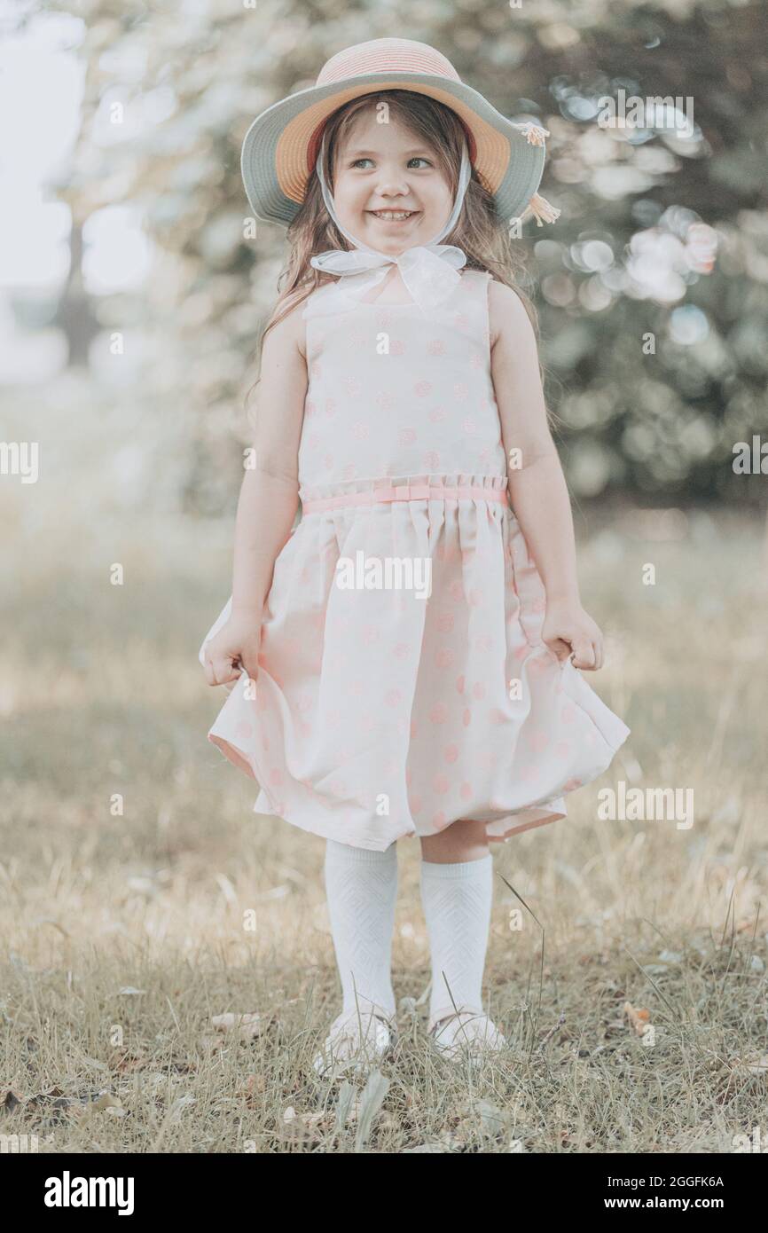 cute little girl in a pink dress with a hat stands in the park in ...