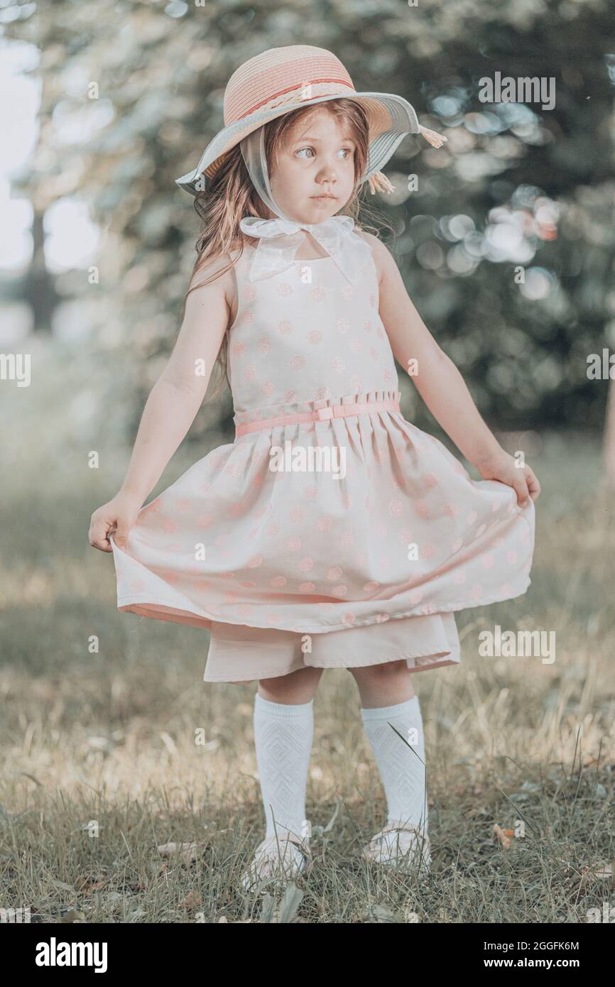 cute little girl in a pink dress with a hat stands in the park in ...