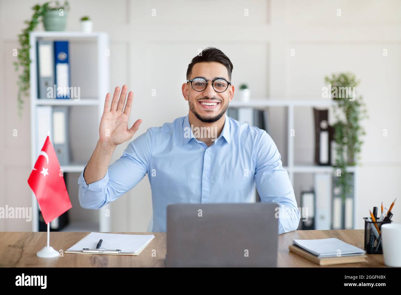Young Arab male teacher with laptop teaching Turkish online from home  office, waving at webcam, greeting students. Confident Eastern tutor giving  educ Stock Photo - Alamy