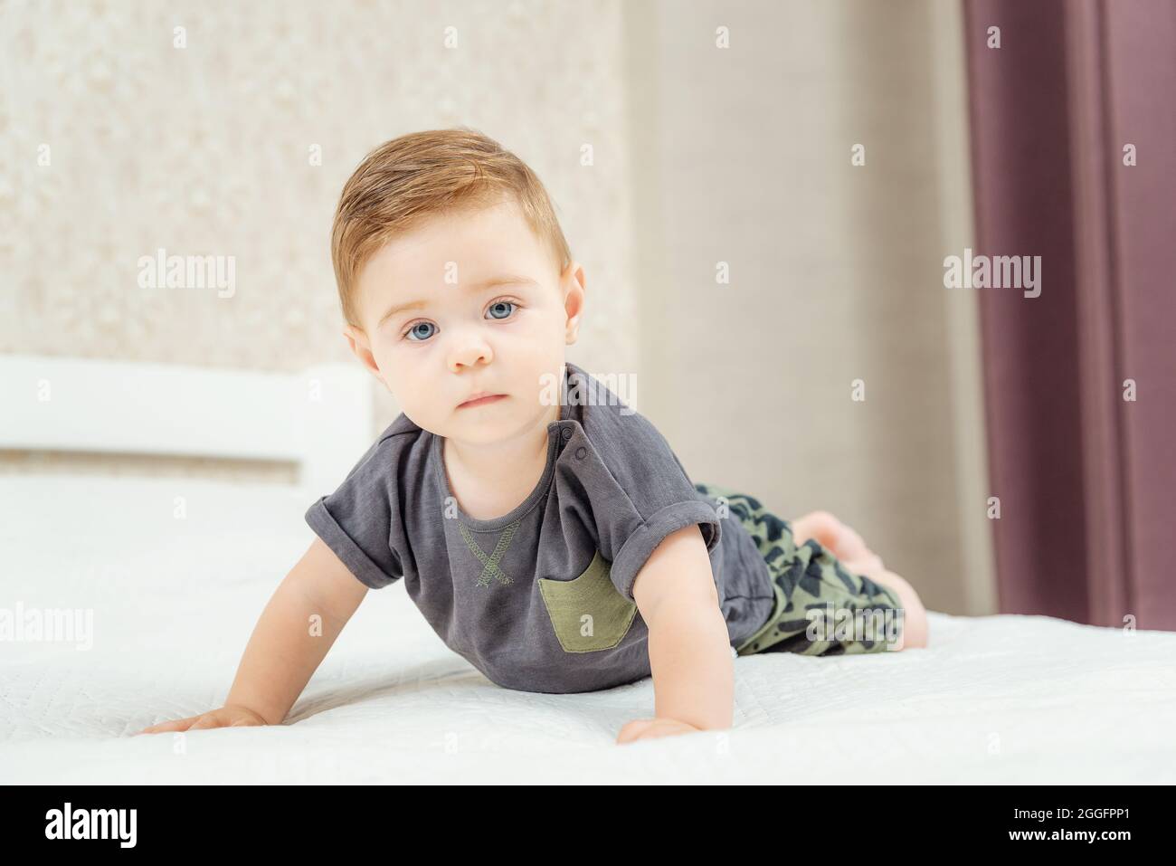 Cute little baby boy lies on a bed and looking at camera ...