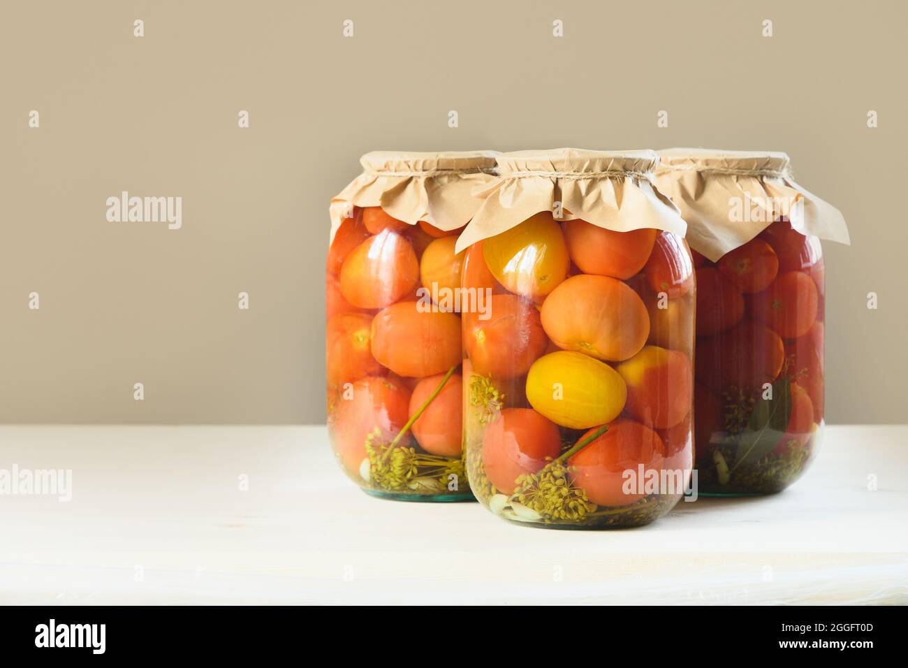 Homemade sour marinated tomatoes in glass jars on beige background. Canned vegetables Stock