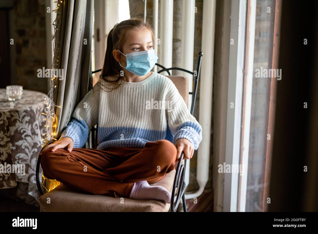 Sad child girl wearing protective mask at home. People coronavirus quarantine concept Stock Photo
