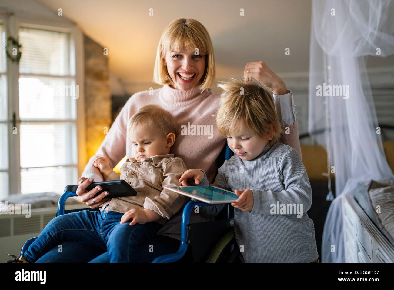 Happy smiling mother with disability in wheelchair playing with children at home Stock Photo
