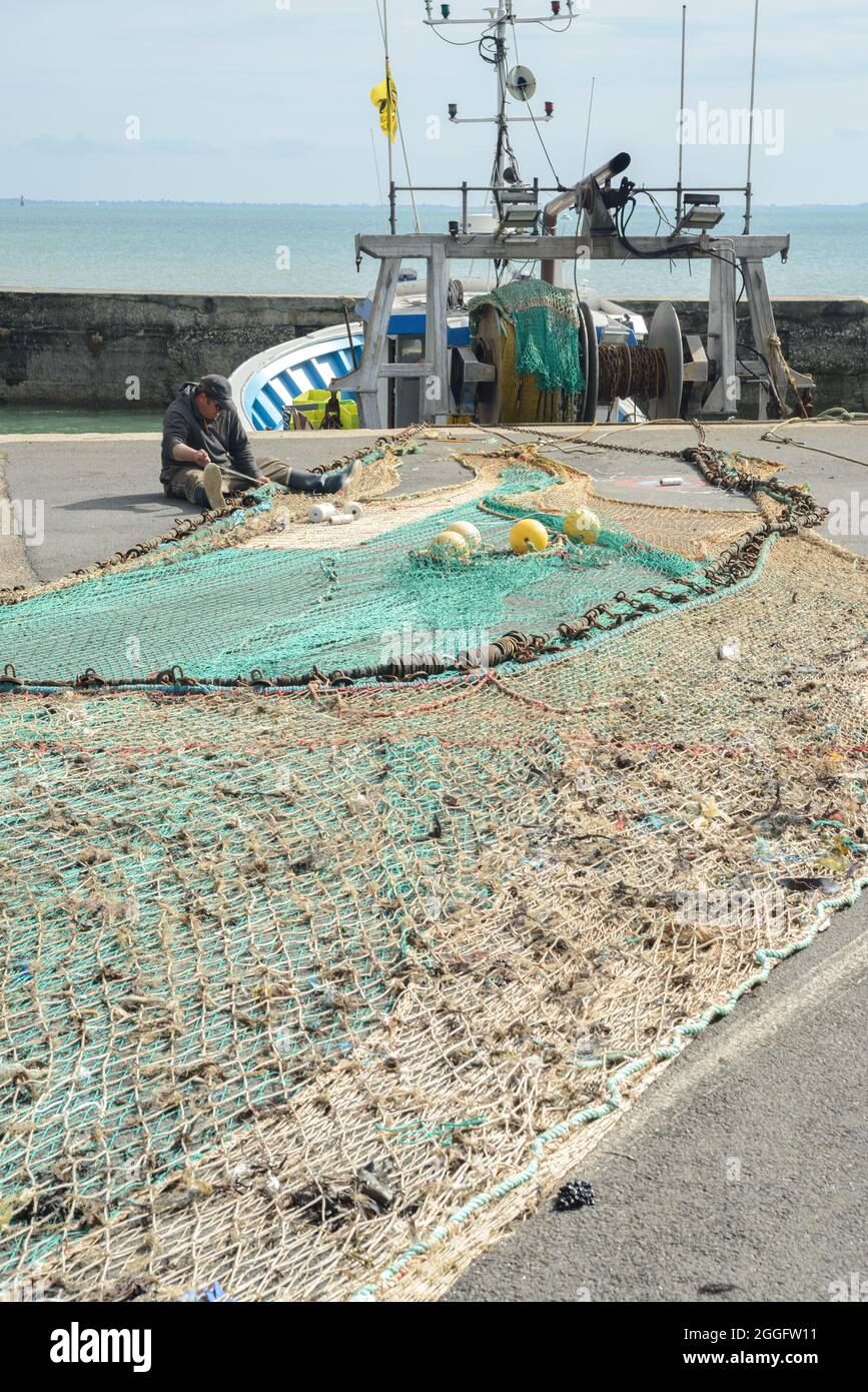 25th April 2015 Oleron Island, Charente Maritime, France - Fishing net spread on harbour quayside at Chateau Oleron and fisherman mending nets Stock Photo