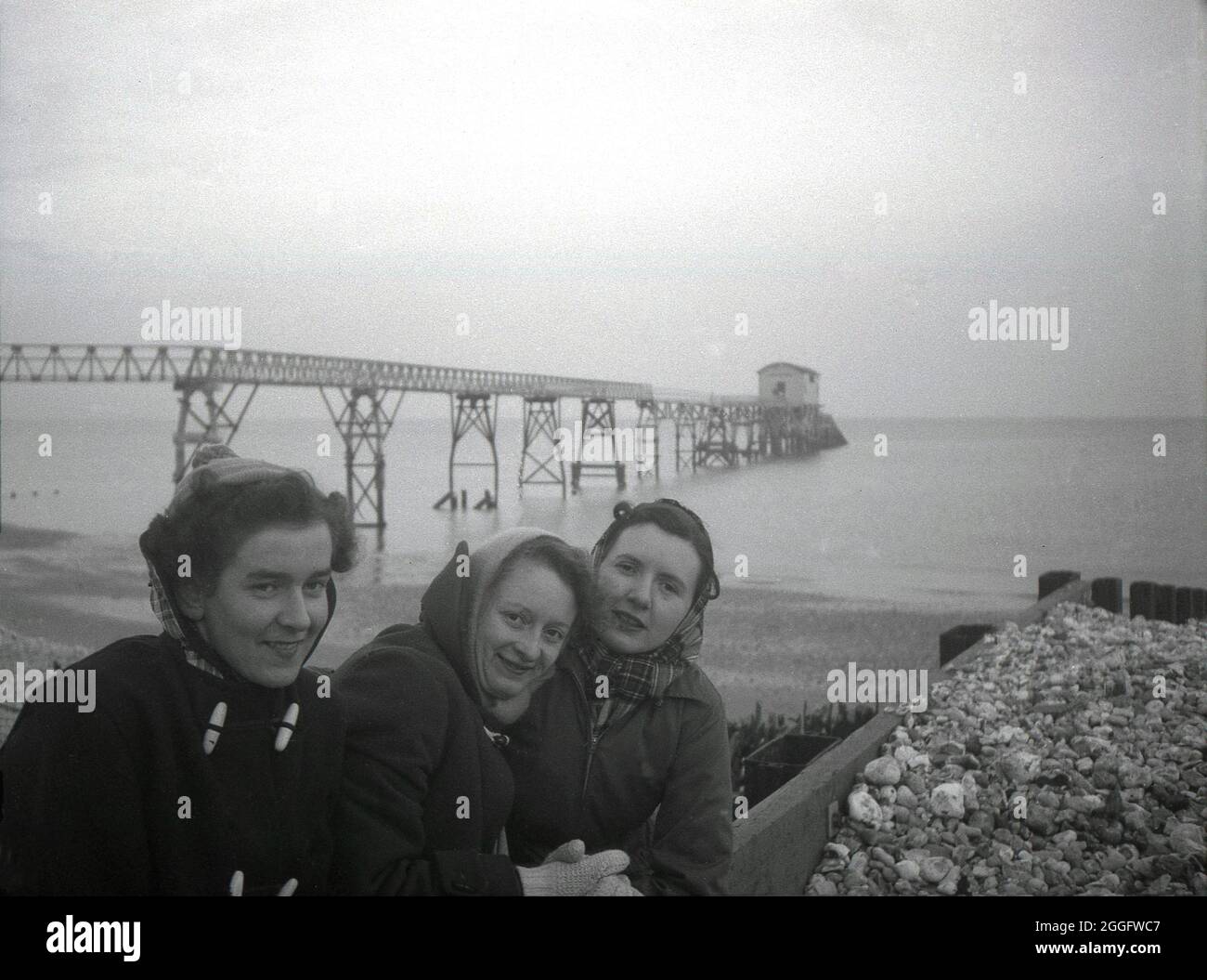1950s, historical, three young ladies on the beach in front of the wooden gangway and old lifeboat station at Selsey, West Sussex, England, UK. A lifeboat service was established in Selsey in 1861. In 1927 to house the station's new motor lifeboat, the boat house was re-built and this structure is seen in the picture. This slipway station was again rebuilt in the late 1950s but was taken down in 2017. Stock Photo