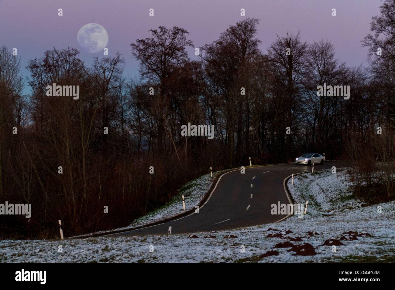 Auto auf einer kurvenreichen Straße mit Schnee und Glatteis bei Vollmond Stock Photo