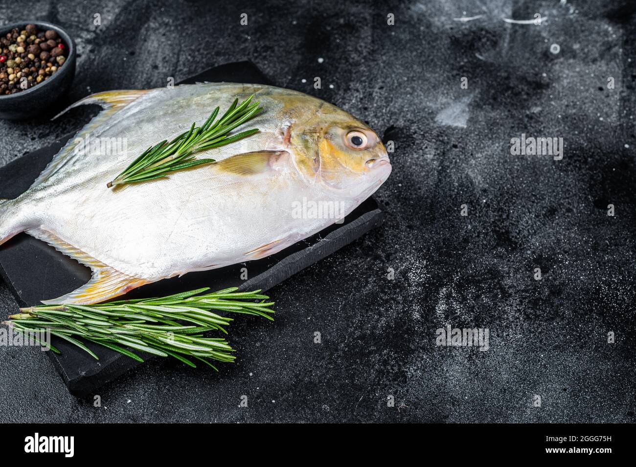 Raw fish pompano with herbs on a marble board. Black background. Top view. Copy space Stock Photo