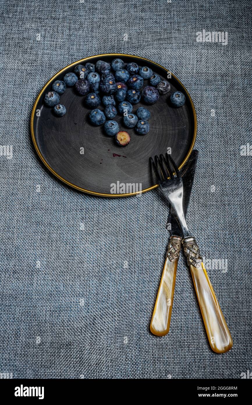 Vintage plate with gold rim with a handful of blueberries inside, fork and knife also in vintage style next to the plate Stock Photo