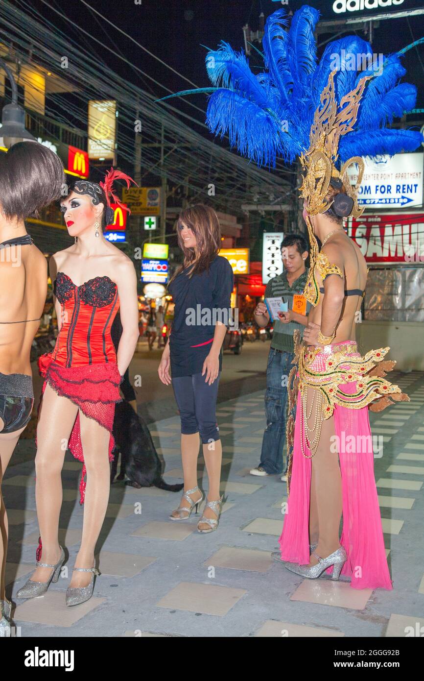 Thai ladyboys dressed in sparkly colourful costumes with flamboyant headdresses stand on street before performing cabaret on stage, Phuket, Thailand Stock Photo