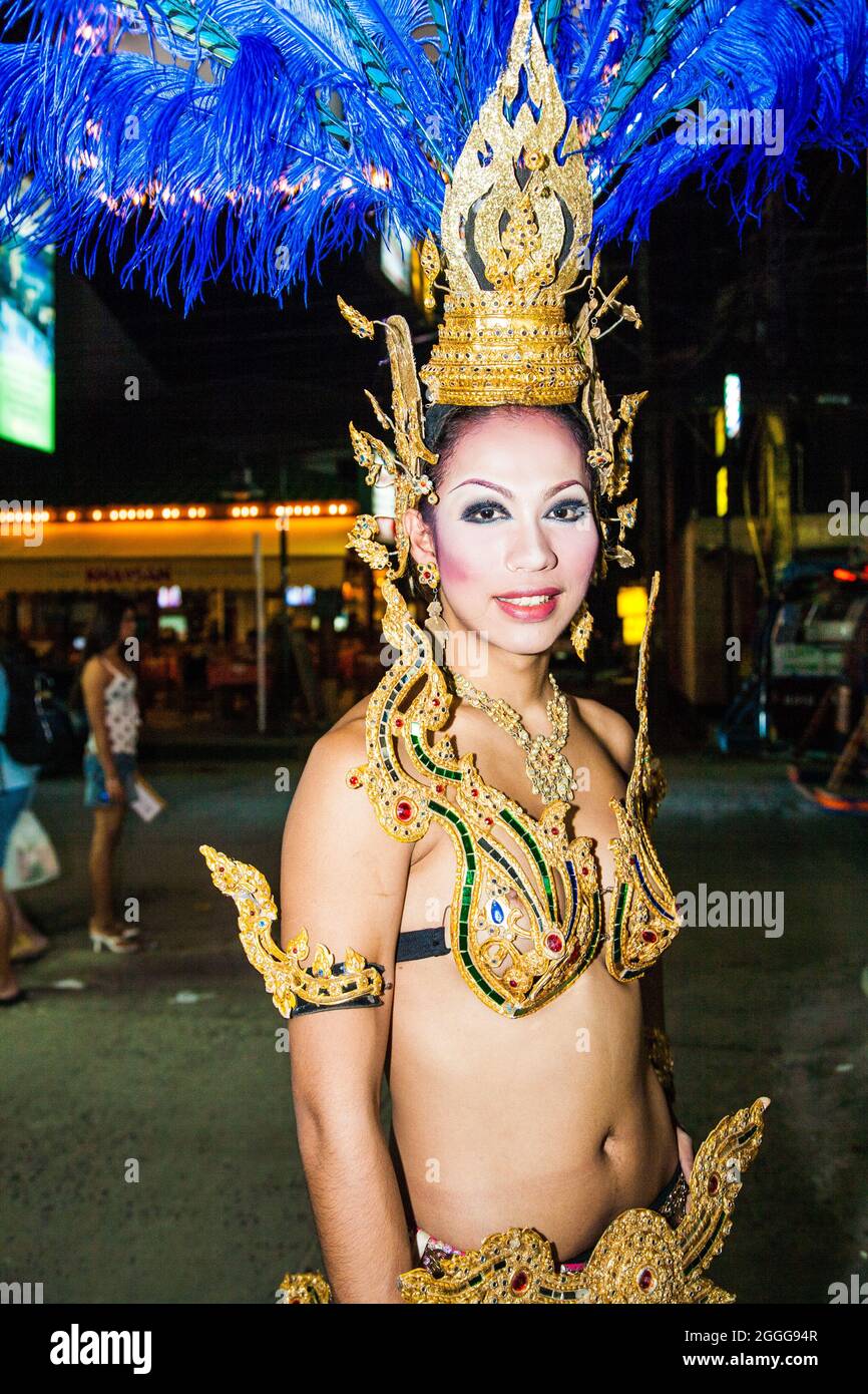 Thai ladyboy dressed in sparkly colourful costume with flamboyant headdress stands on street before performing cabaret on stage, Phuket, Thailand Stock Photo