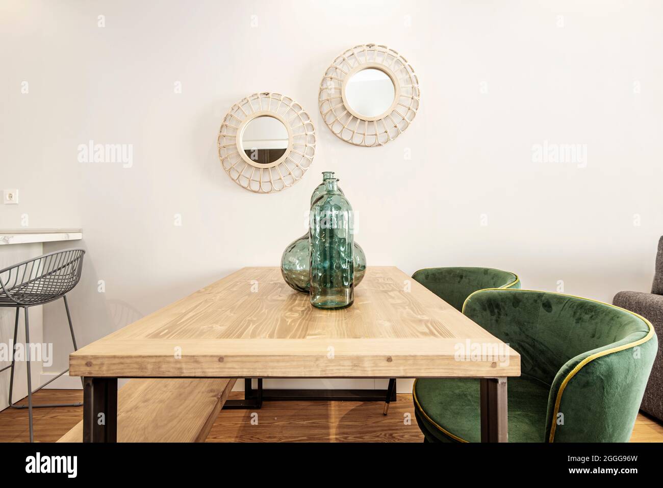 Veined wood table, mirrors on the wall, large vases and green velvet upholstery chairs. Dining room in a vacation rental apartment Stock Photo