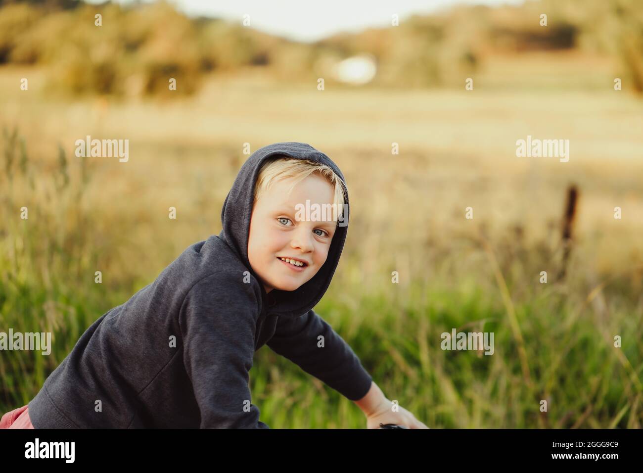 Young blonde boy wearing hoodie riding bike on dry country lane Stock Photo
