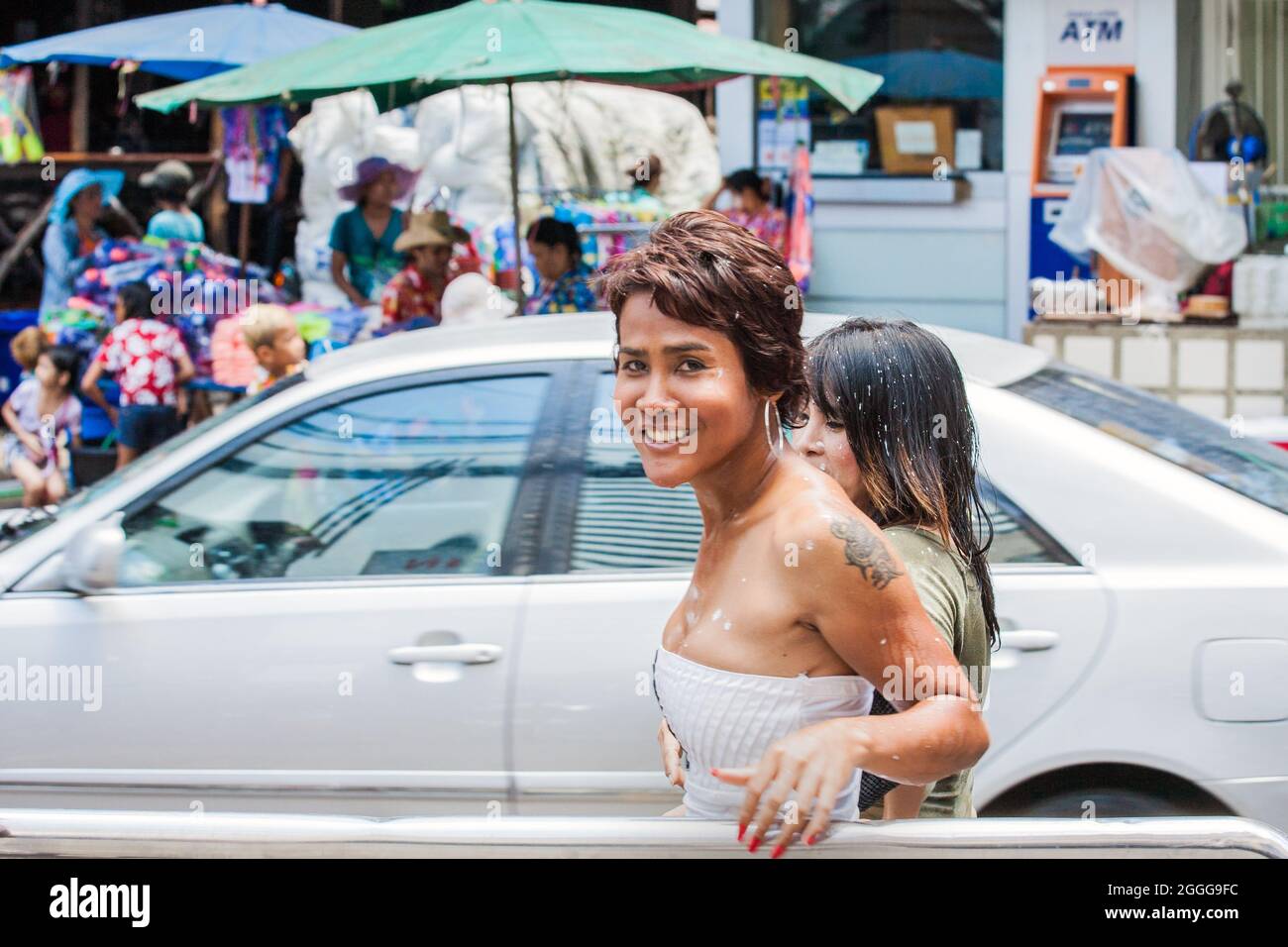 Thai ladyboy with fake boobs and tattoos smiles for photo whilst walking along street during Songkran Festival, Bangkok, Thailand Stock Photo