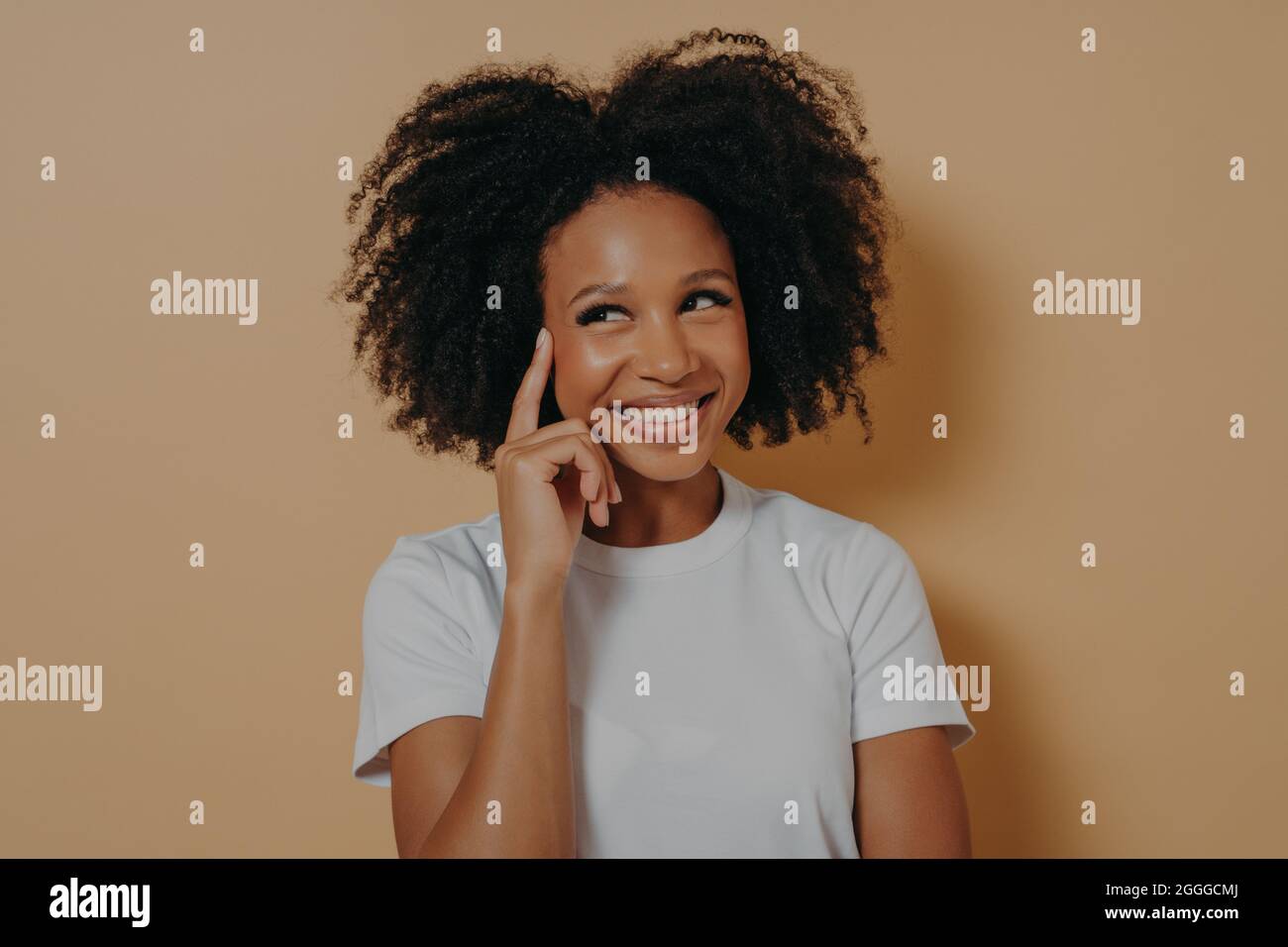 Pensive african woman with curly hair touching temple with forefinger, isolated on beige background Stock Photo