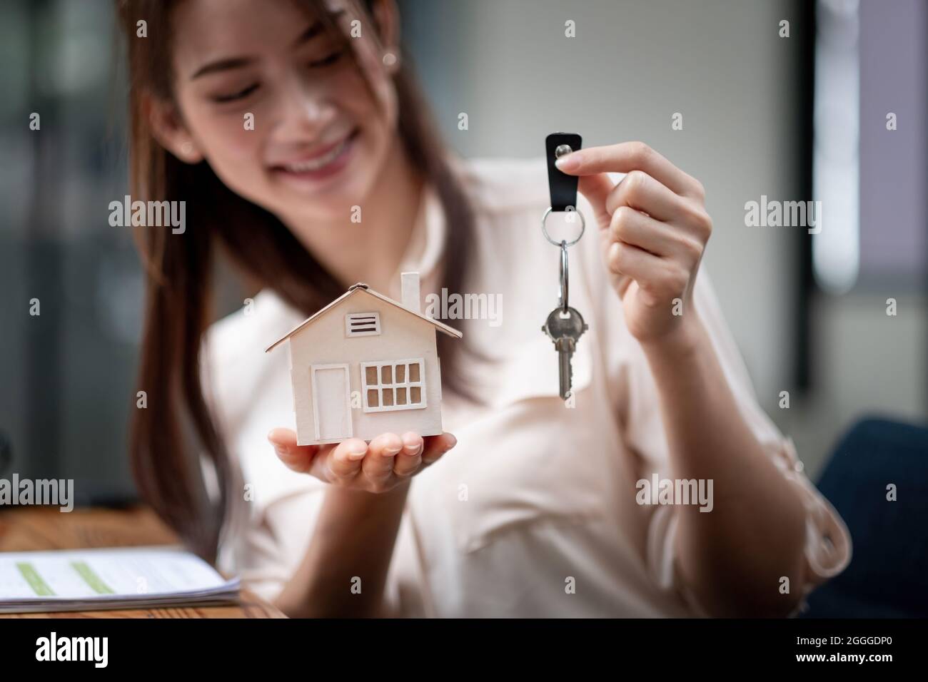 mortgage, real estate and property concept - close up of hands holding house model and home keys at modern office Stock Photo