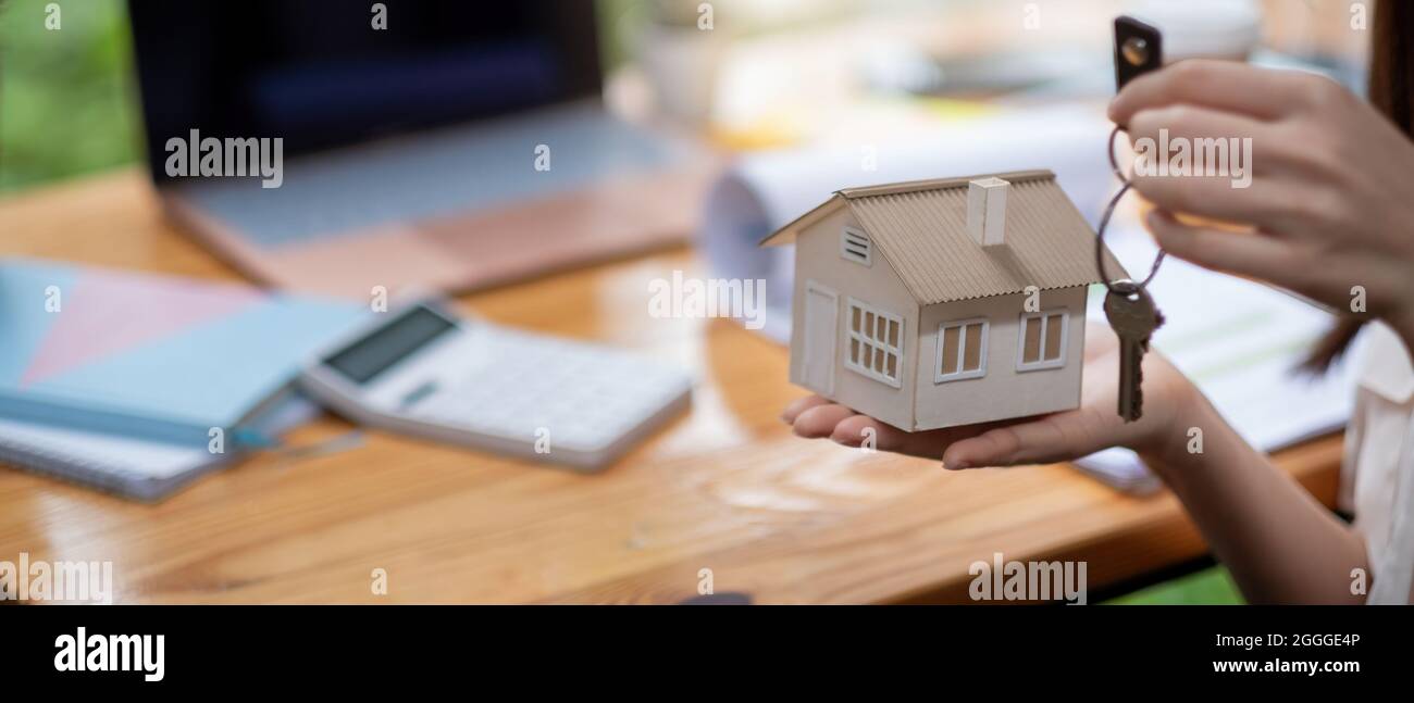 mortgage, real estate and property concept - close up of hands holding house model and home keys with financial working space background. Stock Photo