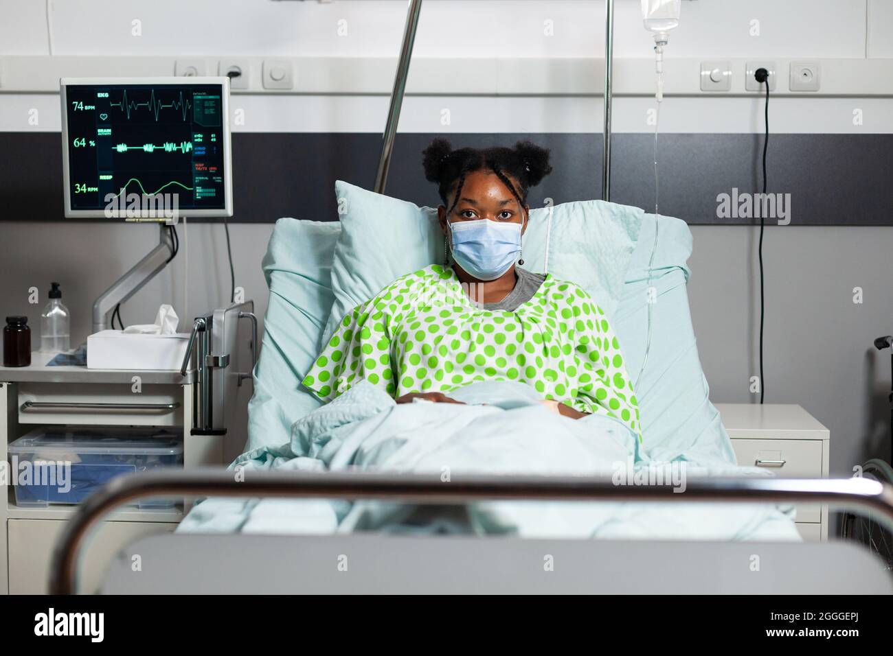 Portrait of young patient with disease sitting in hospital ward at  healthcare clinic. African american sick person with face mask and oximeter  laying in bed with medical equipment Stock Photo - Alamy