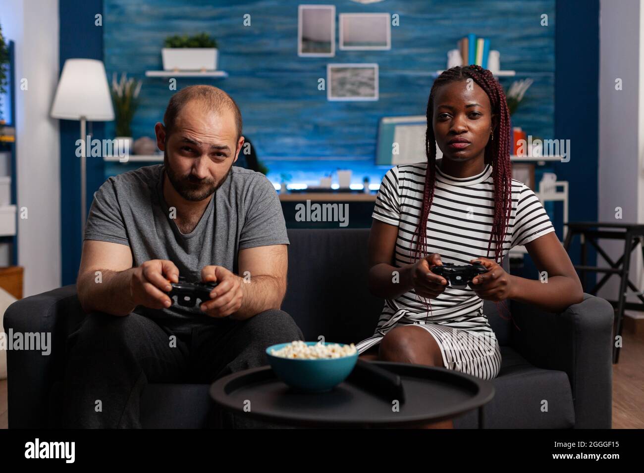 POV of interracial couple playing video game on console holding joysticks at television. Multi ethnic partners looking at camera while enjoying fun activity with technology and controllers Stock Photo