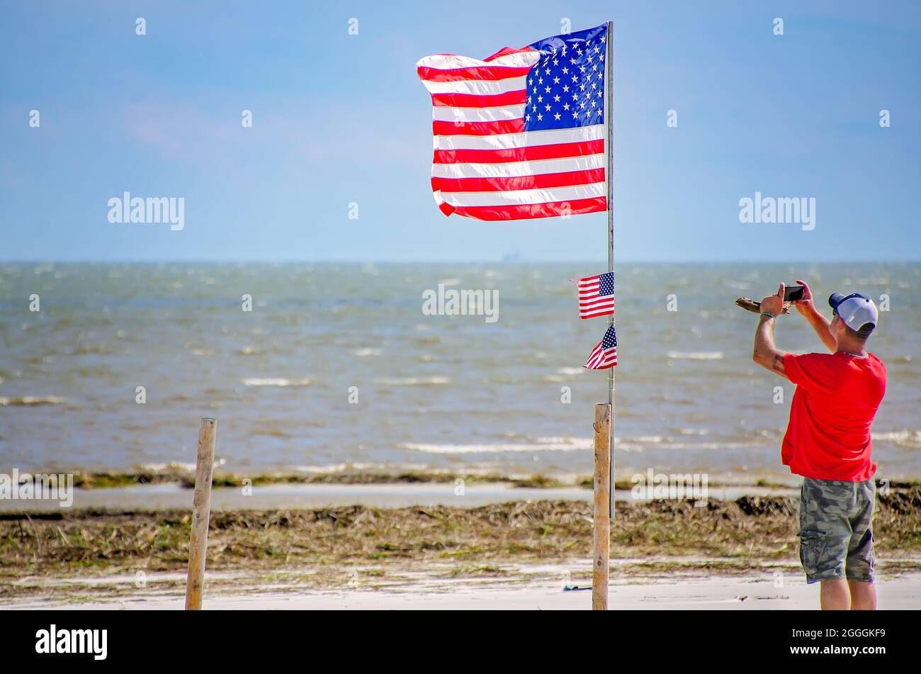 A man uses his cellular phone to photograph an American flag amid debris on the beach after Hurricane Ida, Aug. 31, 2021, in Gulfport, Mississippi. Stock Photo