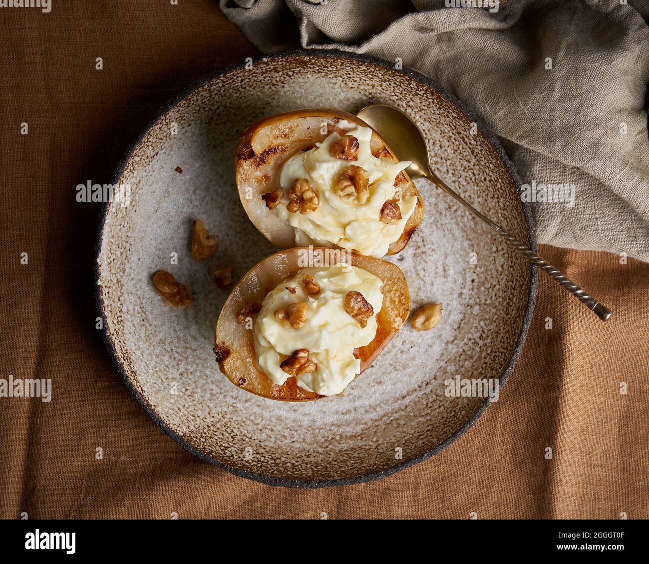 Top view of sliced grilled pears on ceramic plate. Sweet autumn dessert. Walnuts and cream on top Stock Photo