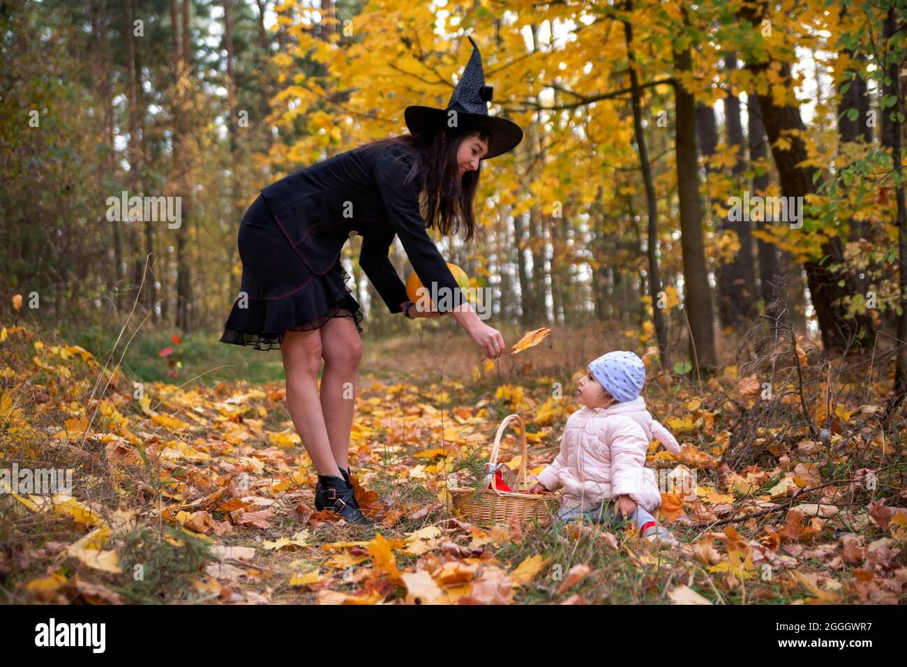 black witch woman with little toddler bunny in the autumn forest. halloween celebration, costume party. Stock Photo