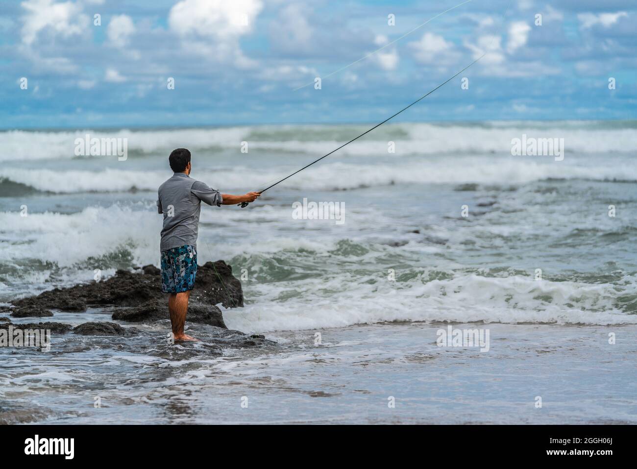 A Costa Rican man wearing a t-shirt and blue shorts is fly fishing at the  beautiful Pacific Coast of Costa Rica. Dramatic cloudy sky on the  background Stock Photo - Alamy